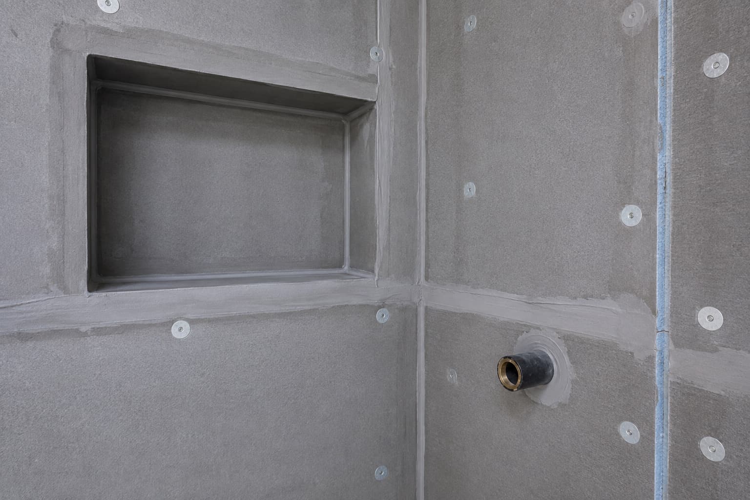 Close view of a sealed shower niche, panel joints, fasteners, and plumbing penetration before tile